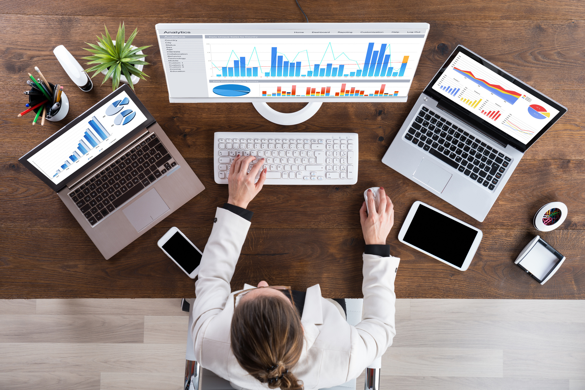 A lady working at her desk with a monitor and 2 laptops