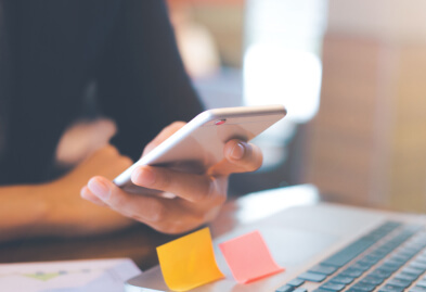 A close up shot of a lady using her phone and a laptop placed on a desk