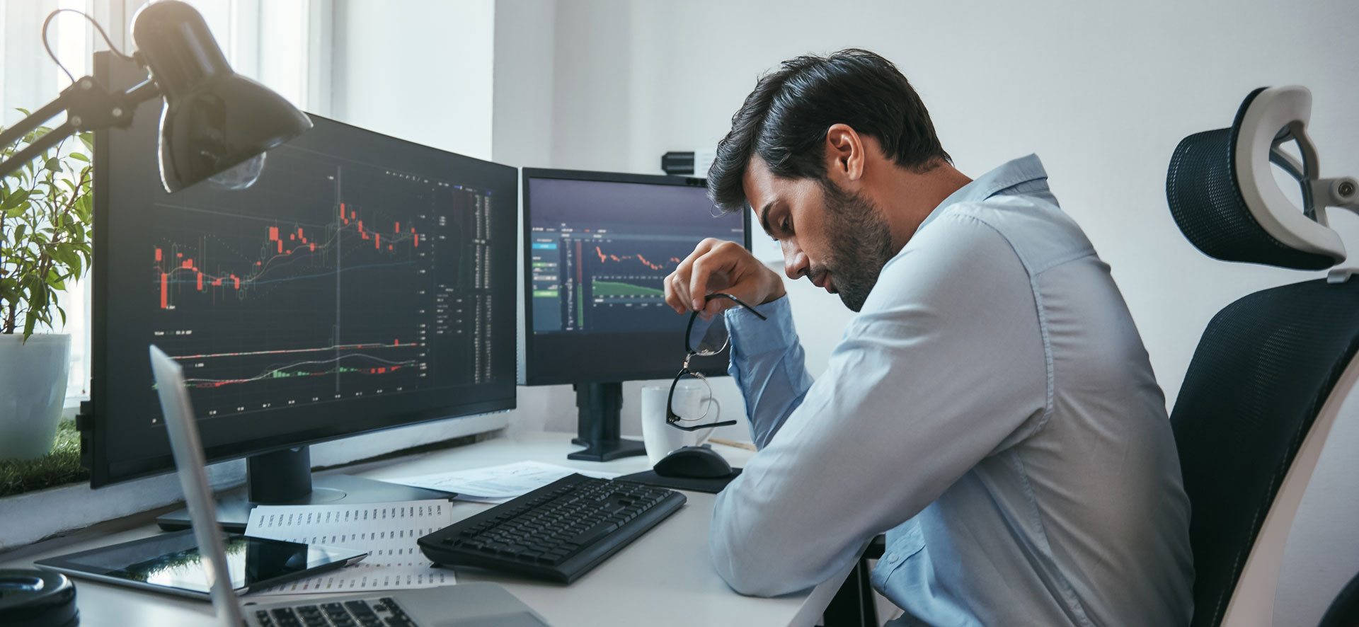 A professional man sitting at his desk in front of two large monitors that display statistics