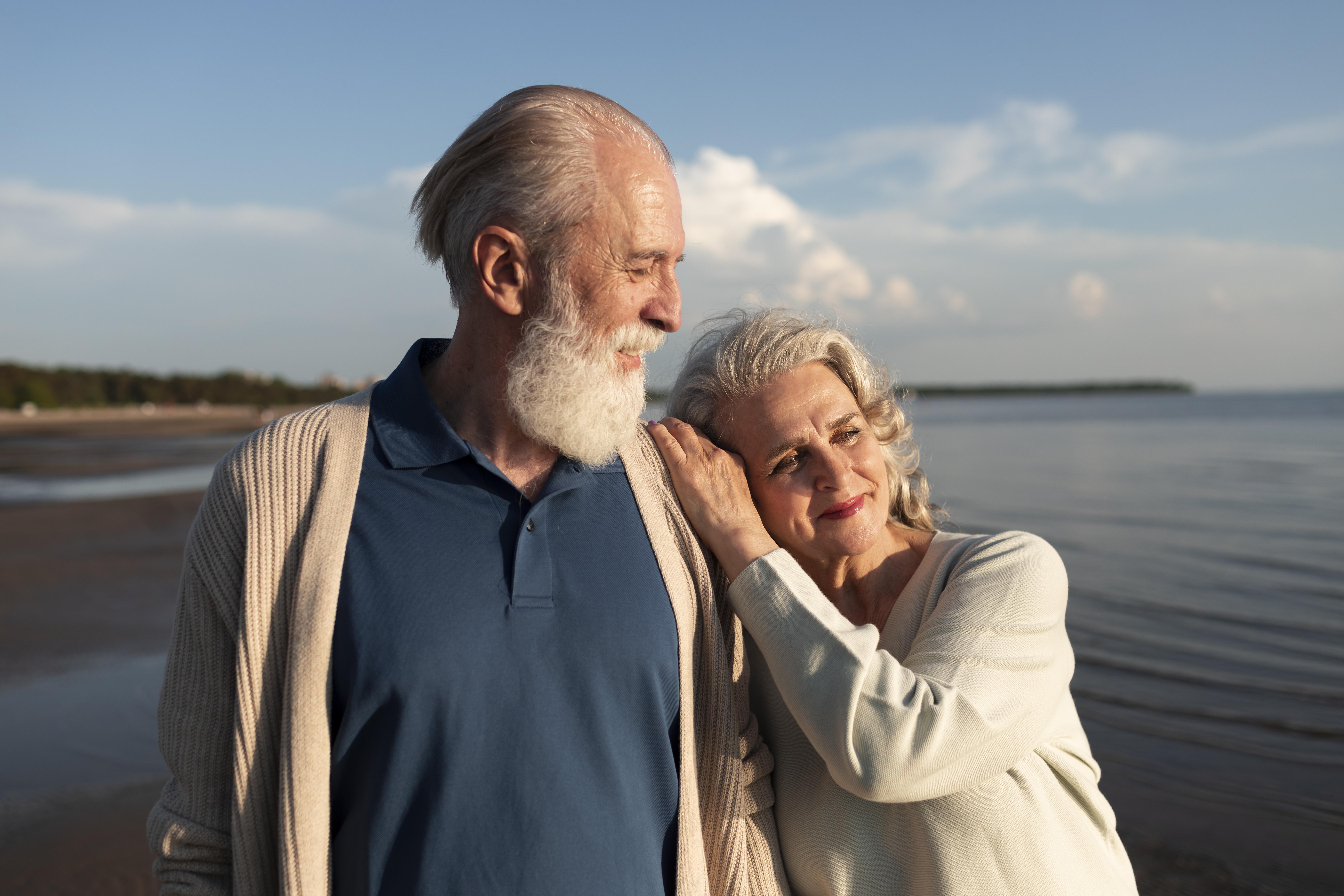 An elderly lady resting her head on the shoulder of her husband by the lakeside